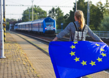 Jeune portant un drapeau europeen sur le quai d'une gare