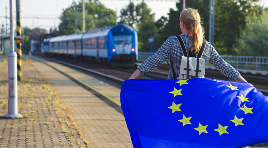 Jeune portant un drapeau europeen sur le quai d'une gare